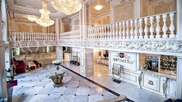 Un lobby de hotel imponente con suelo de mármol, candelabros ornamentados y un balcón con barandillas blancas.