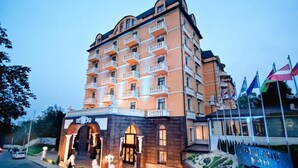 Un hotel de varios pisos con balcones, una entrada de piedra y banderas.
