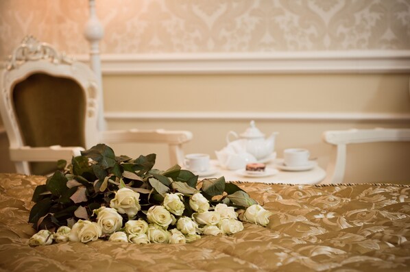 A bed with a bouquet of white roses, a tea set, and a chair in a room with patterned wallpaper.