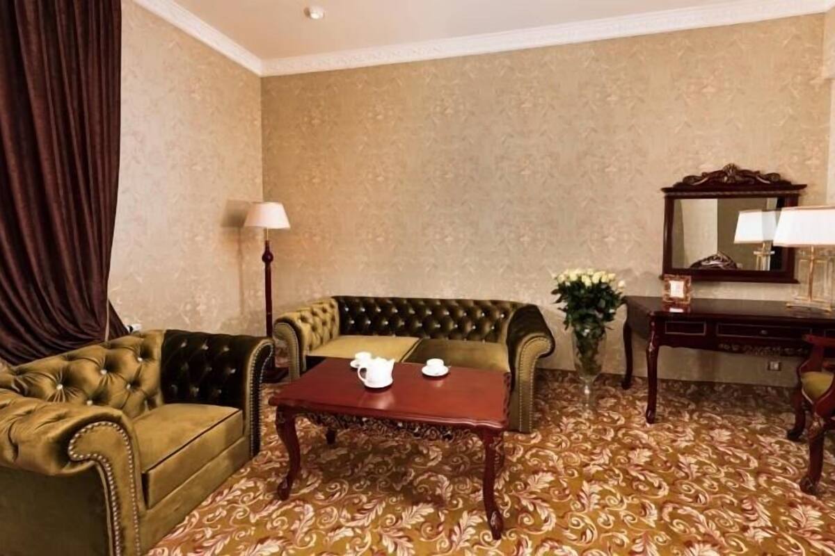 A room with a tufted sofa, a small table with a teapot, a lamp, and a mirror.