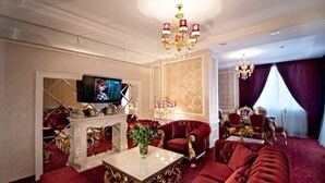 Una sala de estar lujosa con chimenea, sofás rojos, televisor y candelabro.