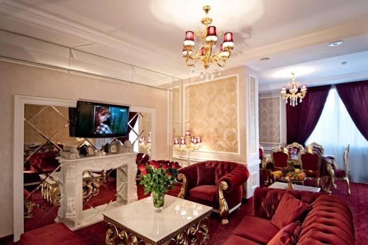 A luxurious living room with a fireplace, red sofas, a television, and a chandelier.