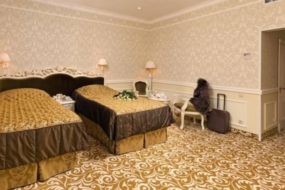 A hotel room with two beds, a chair, a desk, and a suitcase.