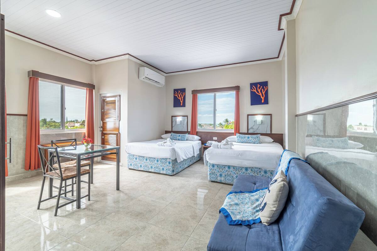 A hotel room with two beds, a dining table, and a sofa.