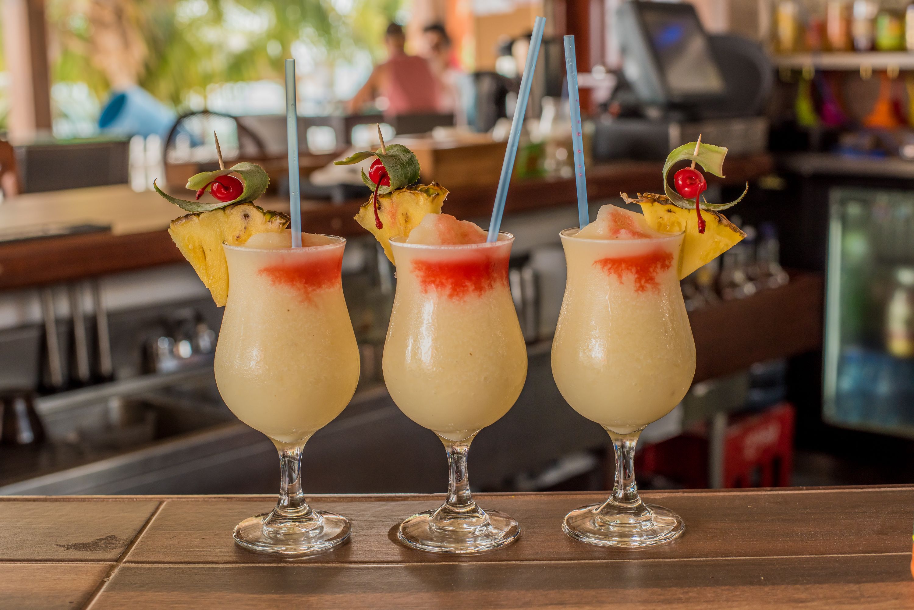 Drei Cocktails mit Obstgarnituren auf einer Bar.