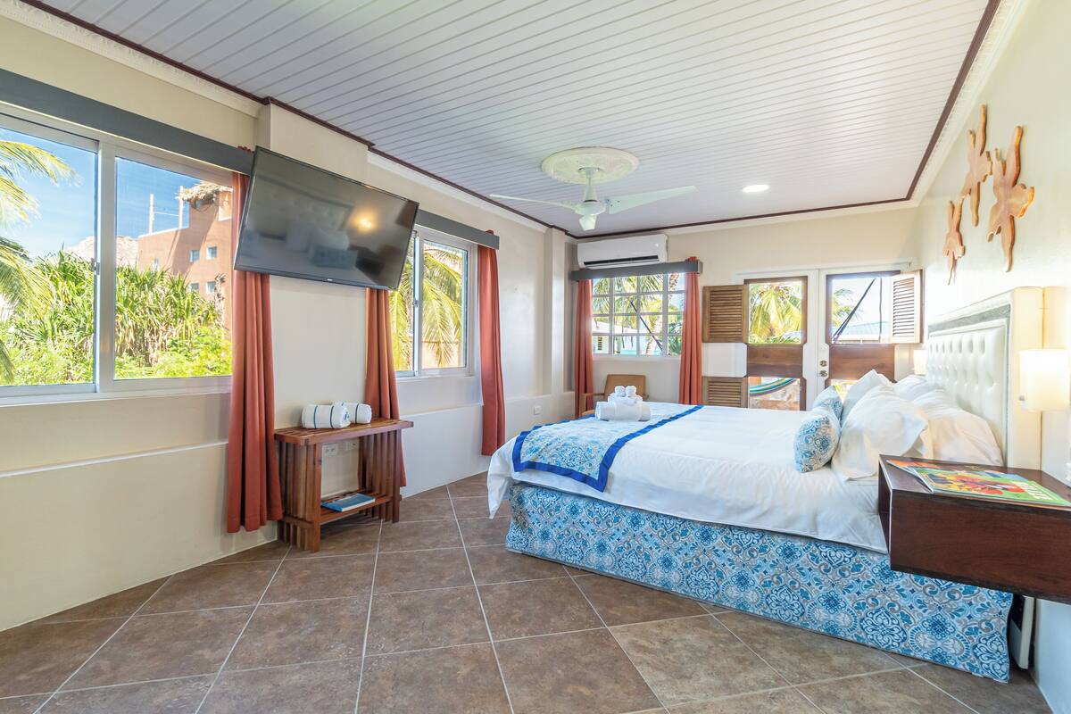 A hotel room with a bed, a TV, a ceiling fan, and a window with curtains.