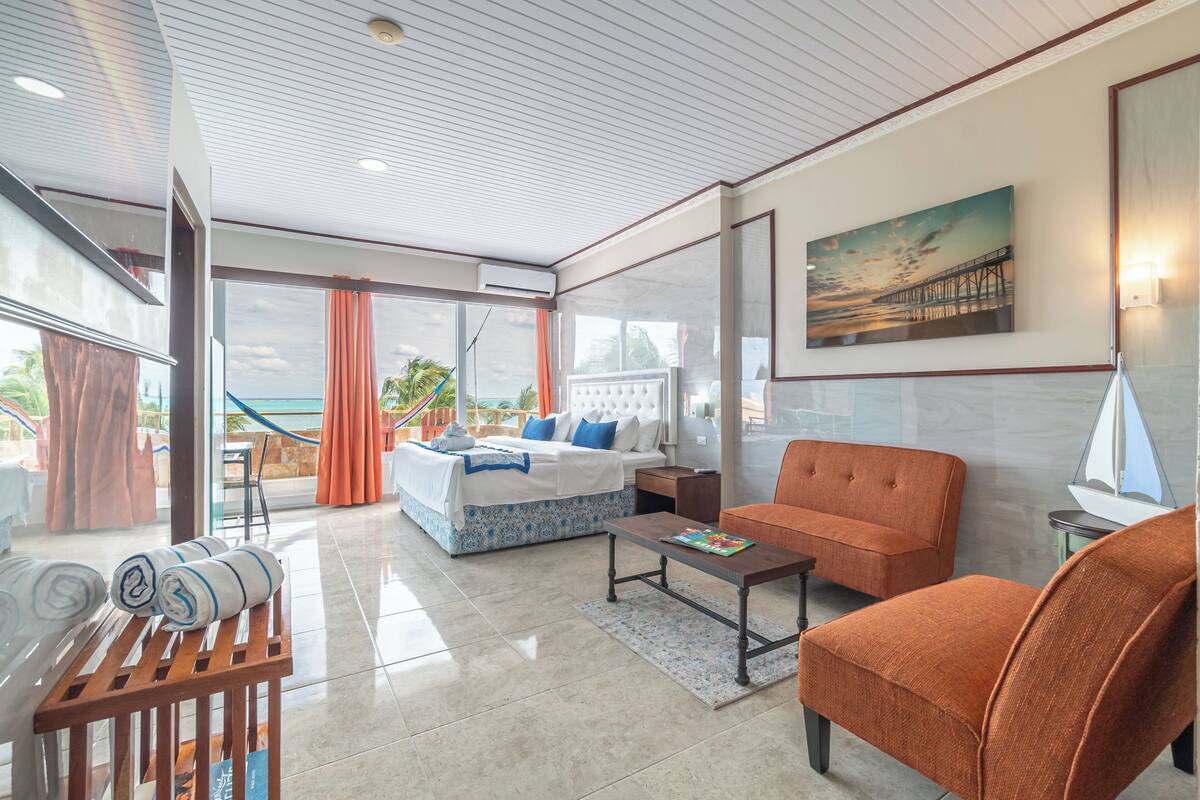 A modern hotel room with a bed, orange sofa, and a view of the ocean.