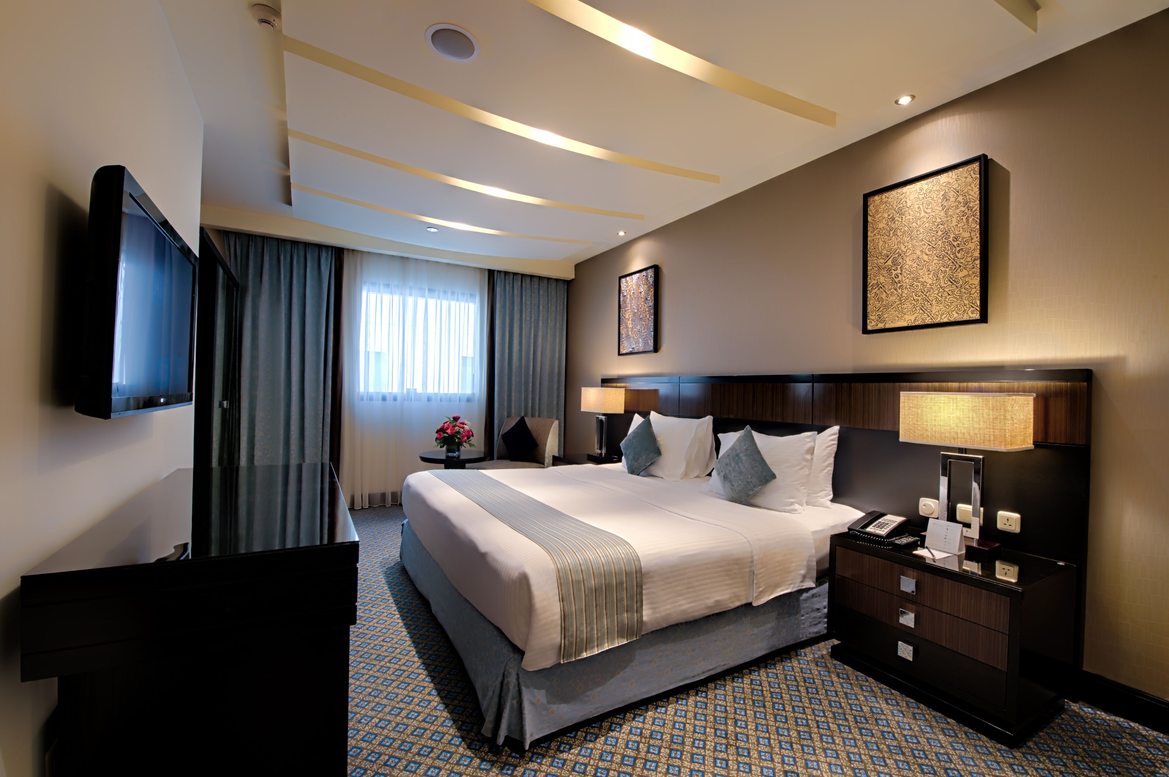 A hotel room with a large bed, a television, a desk with a lamp, and a nightstand with a phone.
