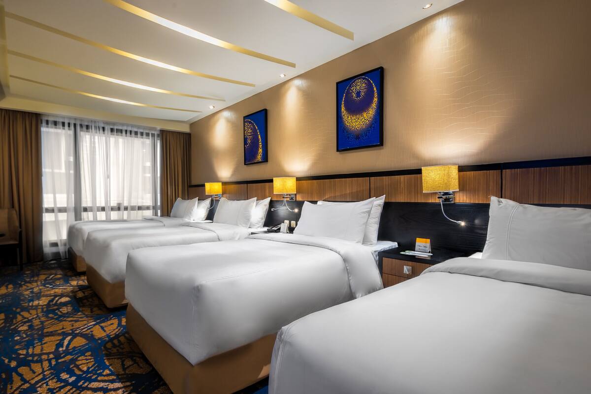 A hotel room with three beds, a large window with sheer curtains, and a patterned carpet.
