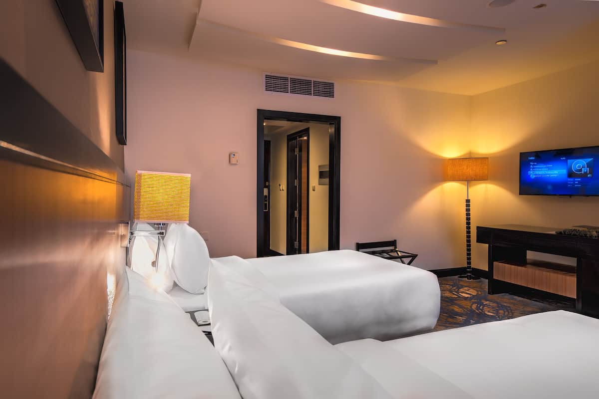 A hotel room with two beds, a television, a desk, and a lamp.
