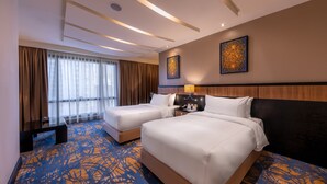 A hotel room with two beds, a large window with curtains, a wall-mounted artwork, and a patterned carpet.