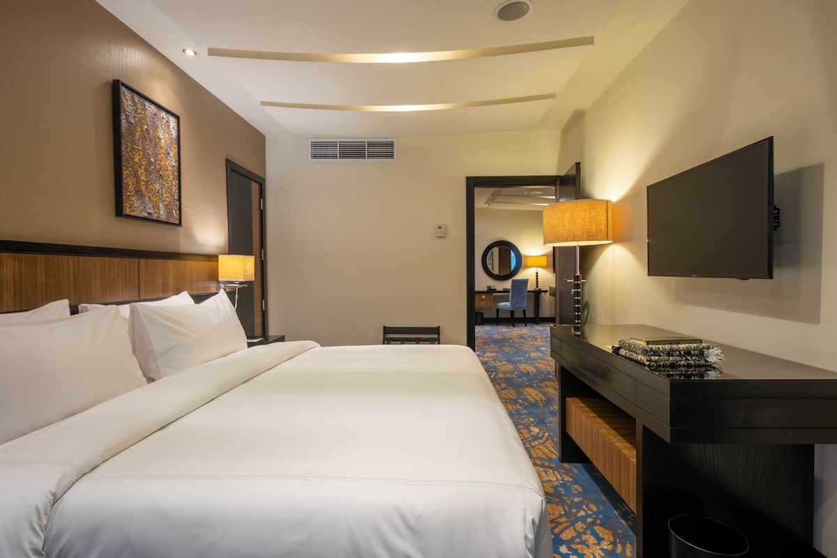 A hotel room with a large bed, a desk, a television, and a bathroom visible through an open door.