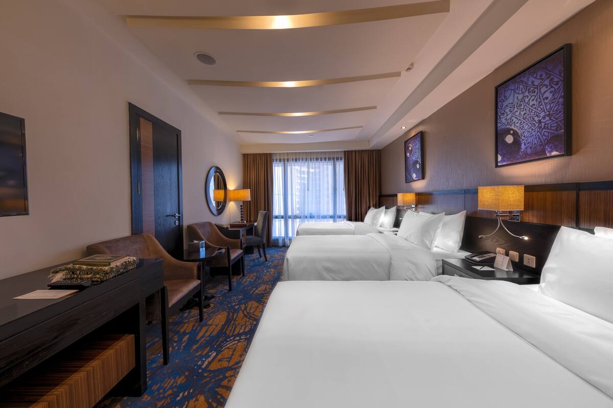 A hotel room with two beds, a desk, a chair, and a large window with curtains.