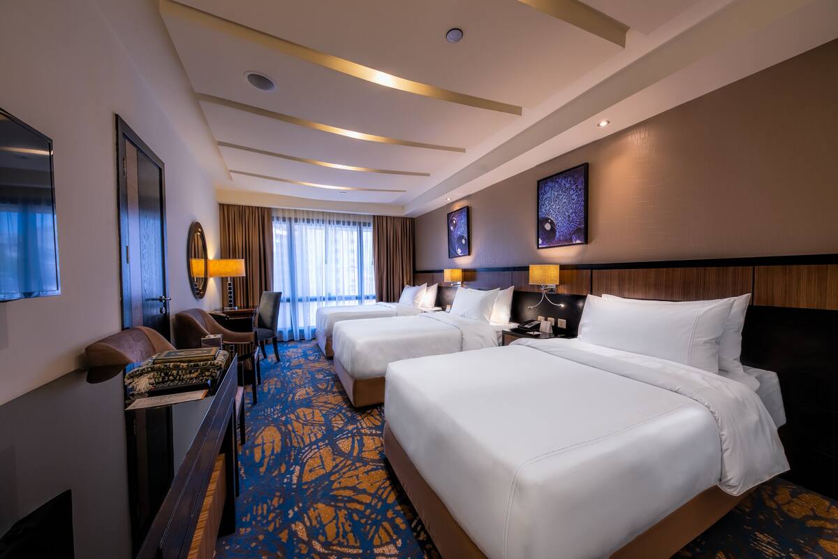 A hotel room with two beds, a desk, a chair, and a large window with curtains.
