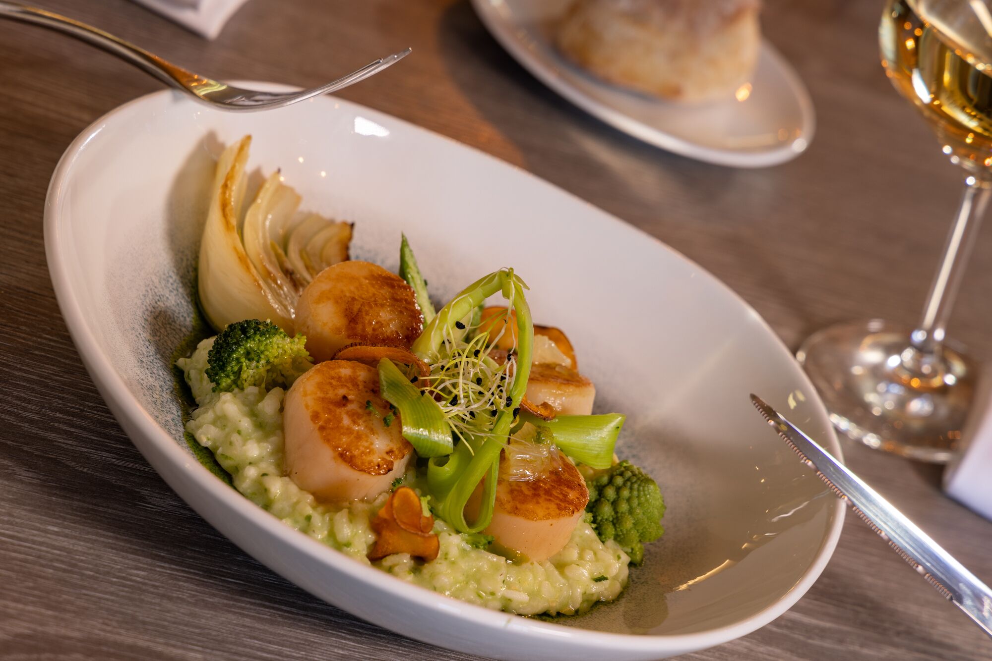 Un piatto con capesante grigliate, broccoli e risotto cremoso.