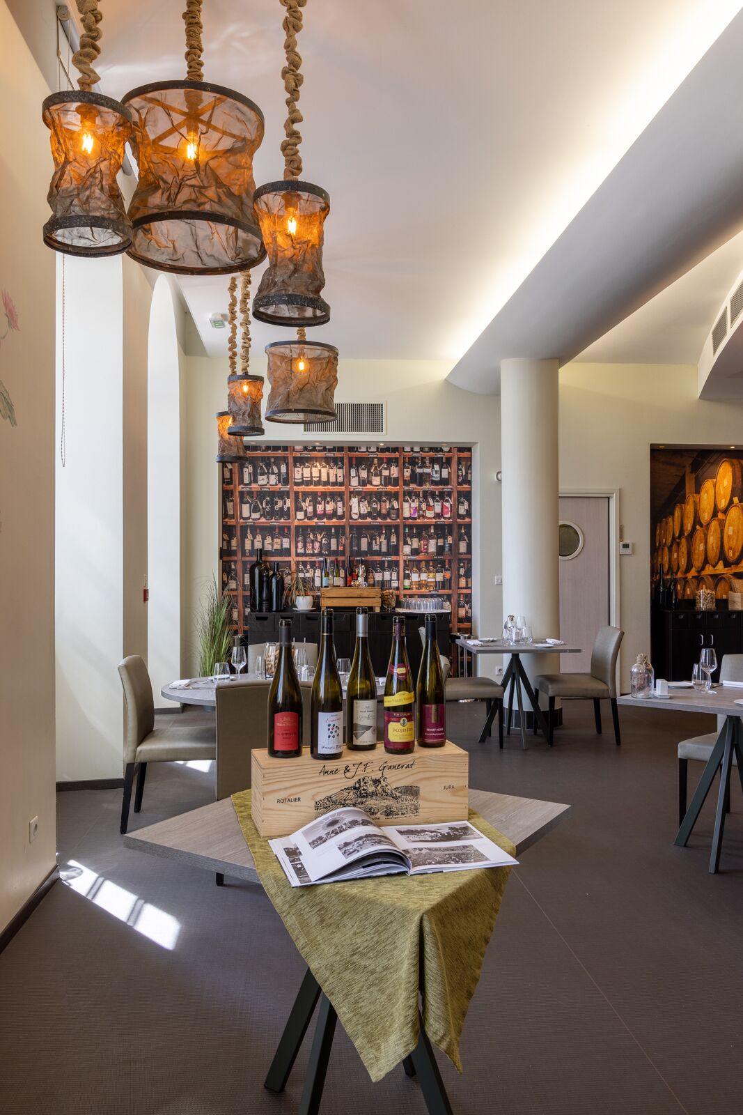 Un restaurante con una vitrina de vinos, luces colgantes y una mesa con botellas de vino.