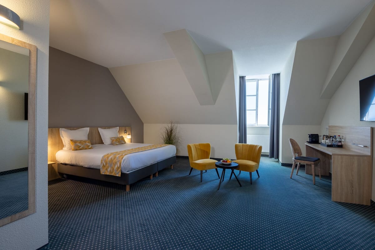 Ein Hotelzimmer mit einem Bett, zwei gelben Sesseln, einem Schreibtisch und einem Fernseher.