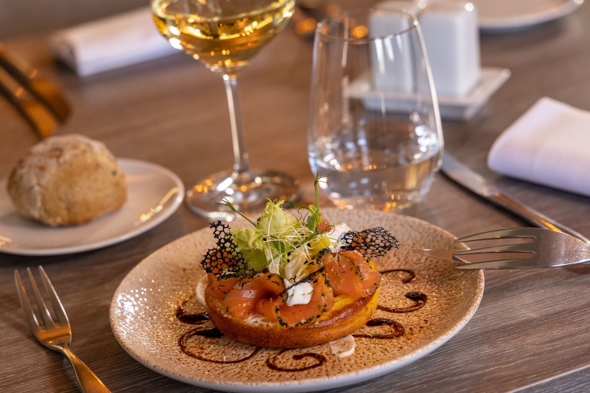A plate with a food item, a glass of white wine, and a water glass on a wooden table.