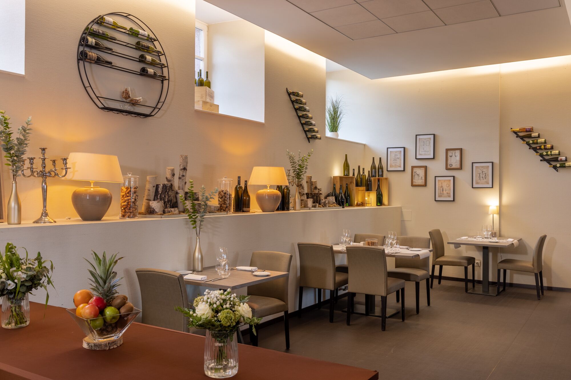 A restaurant interior with a bar area, multiple tables, chairs, and a variety of wine bottles displayed on shelves.