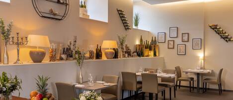 A restaurant interior with a bar area, multiple tables, chairs, and a variety of wine bottles displayed on shelves.