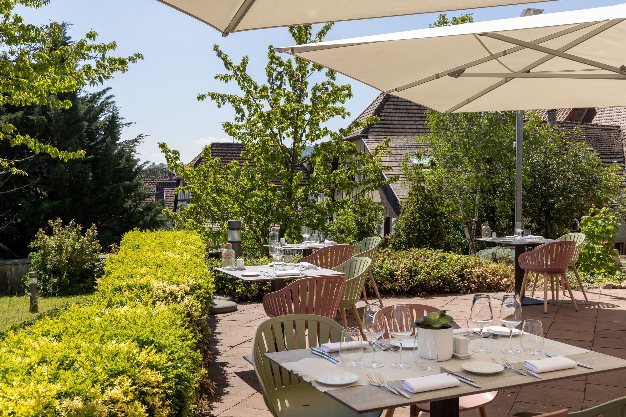 Eine Terrassensitzgruppe mit Tischen und Stühlen, umgeben von Grünflächen und Gebäuden.