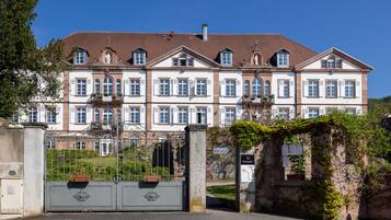 Ein großes, mehrgeschossiges Gebäude mit einer symmetrischen Fassade, das einen zentralen Eingang mit einem schmiedeeisernen Tor und einer Steinsäule zeigt.