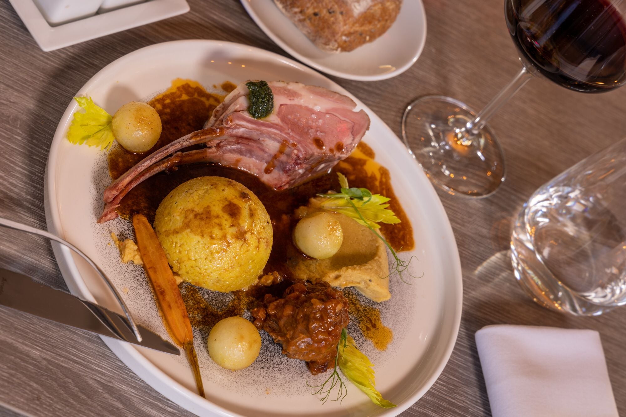 A plate of food with a lamb shank, potatoes, and a sauce.