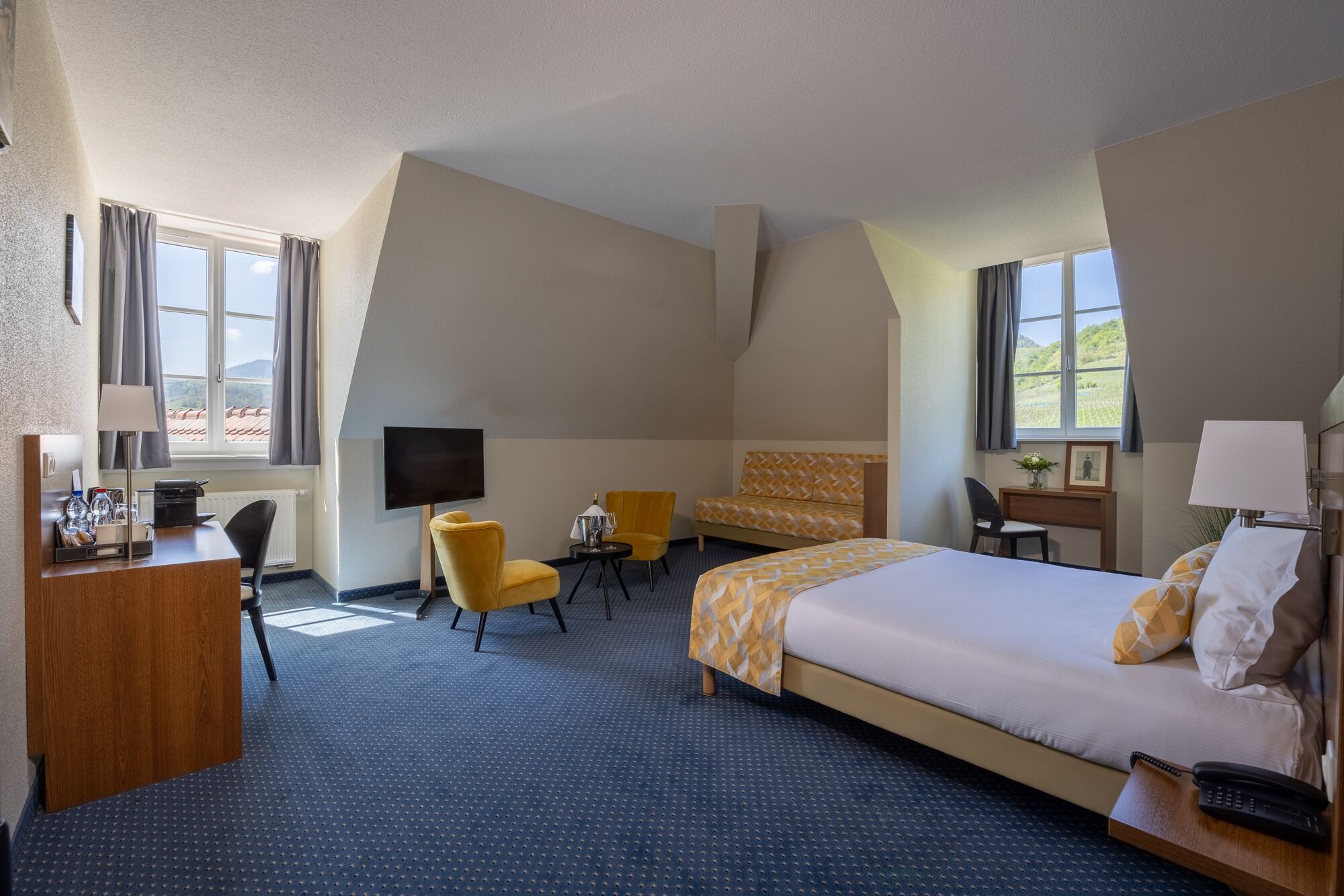 Habitación de hotel con una cama grande, un escritorio, una silla, un televisor y una ventana con cortinas.