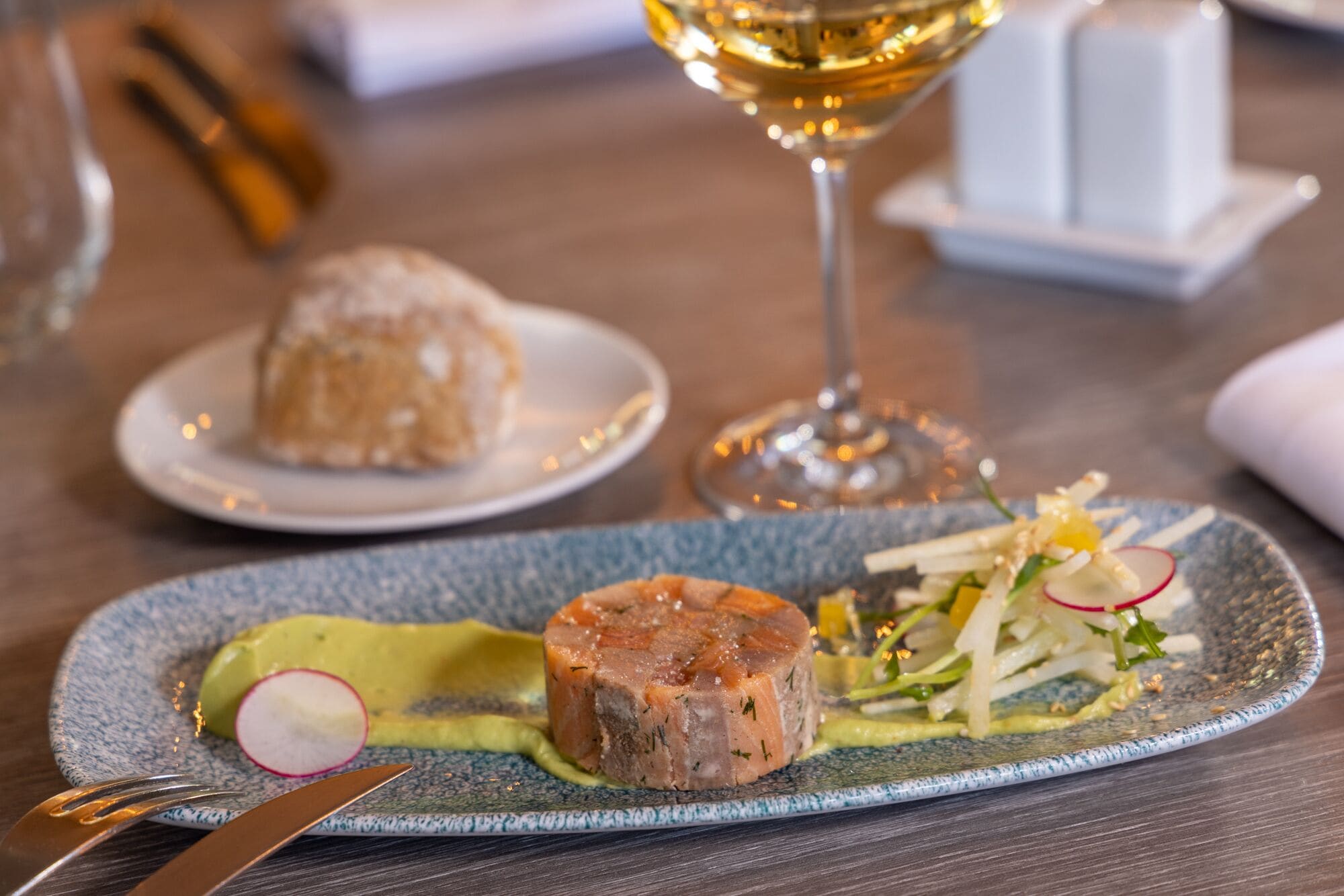 A dining table with a plate of food, a glass of wine, and a fork.