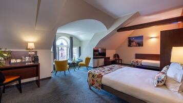A hotel room with a bed, desk, chair, and a view of a building through a window.