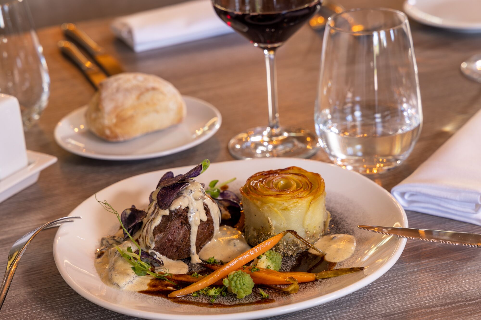 A plate of food with a steak, vegetables, and a pastry on a wooden table.