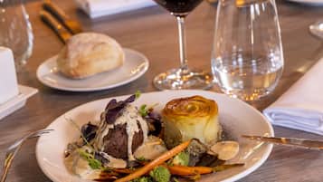 A plate of food with a steak, vegetables, and a pastry on a wooden table.