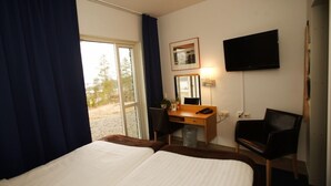 Una habitación de hotel con dos camas, un escritorio con silla, televisor y ventana con cortinas.