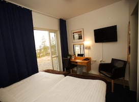 Quarto de hotel com duas camas, uma escrivaninha com cadeira, televisão e janela com cortinas.