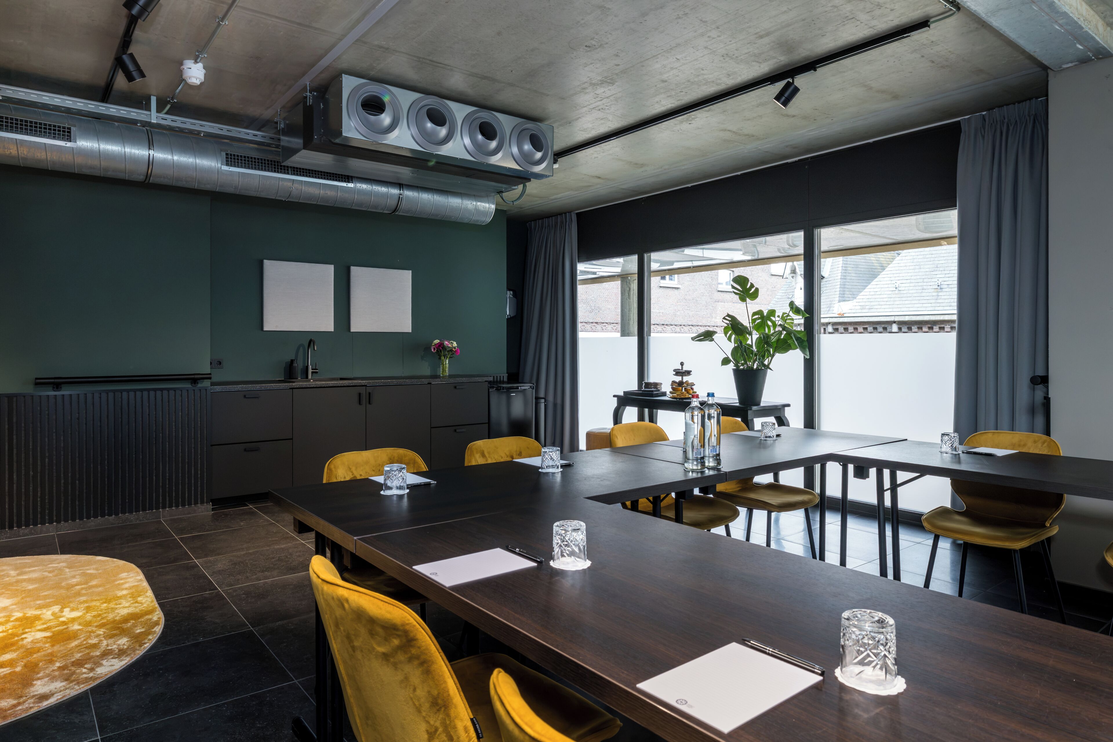 A conference room with a long table, yellow chairs, a potted plant, and a view of the outside.