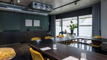 A conference room with a long table, yellow chairs, a potted plant, and a view of the outside.