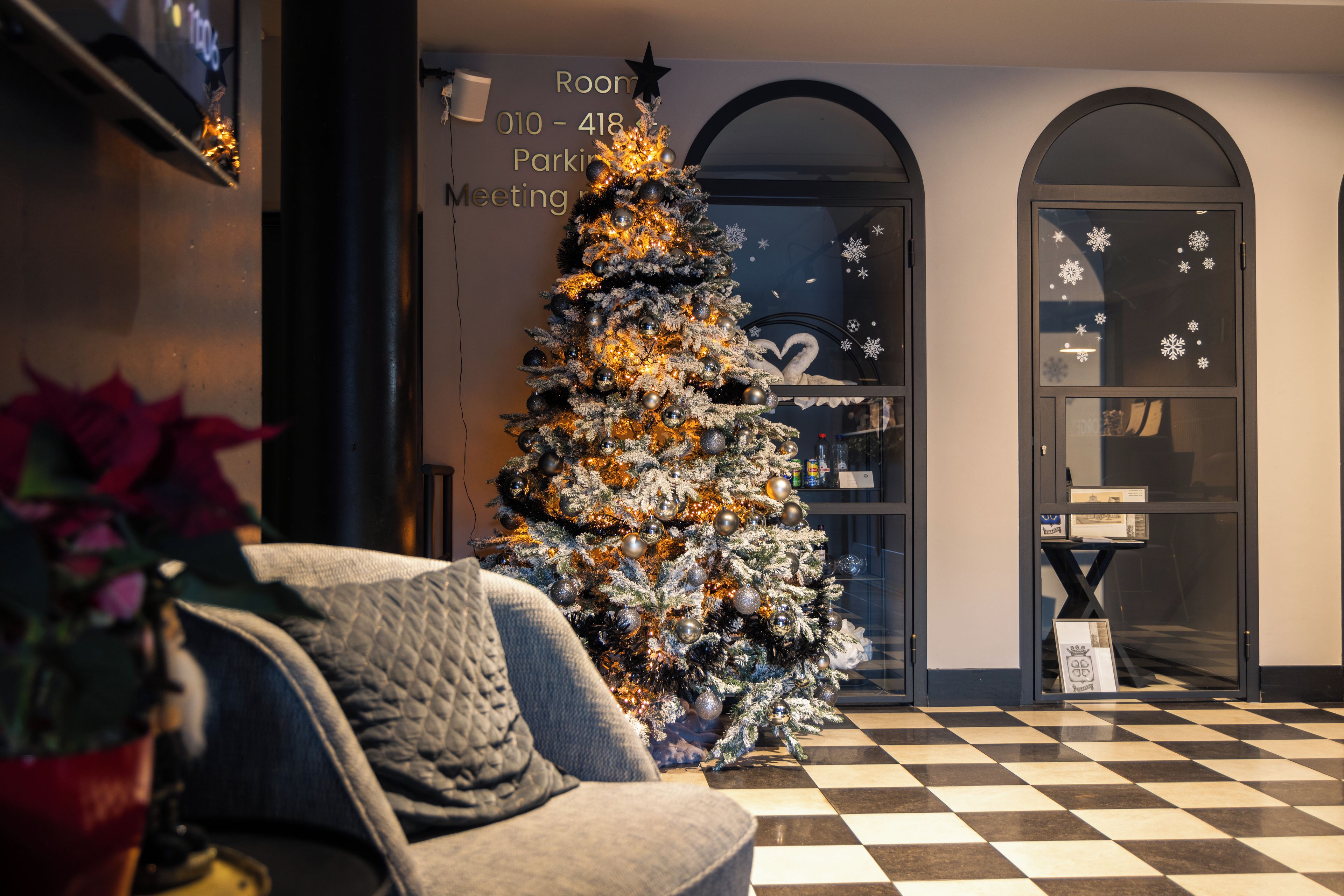Árvore de Natal em um hall com piso xadrez e placa indicando uma sala de reuniões.