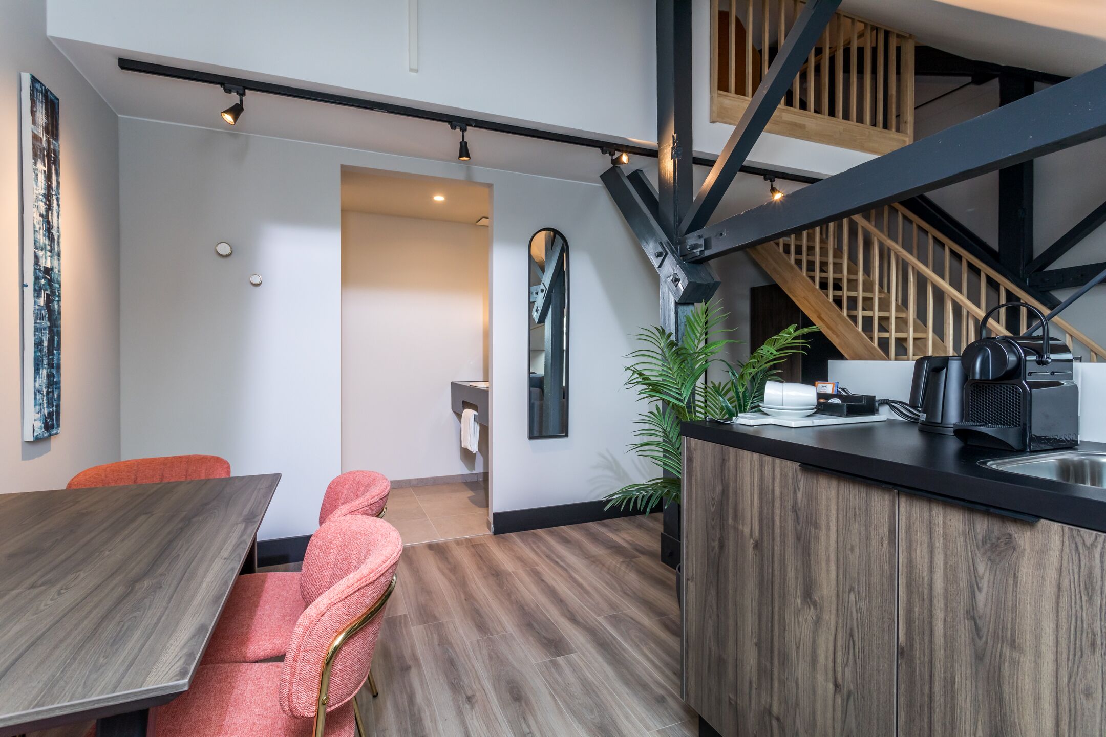 A modern kitchen with a wooden countertop, a sink, and a coffee maker. There is a staircase leading to an upper level.