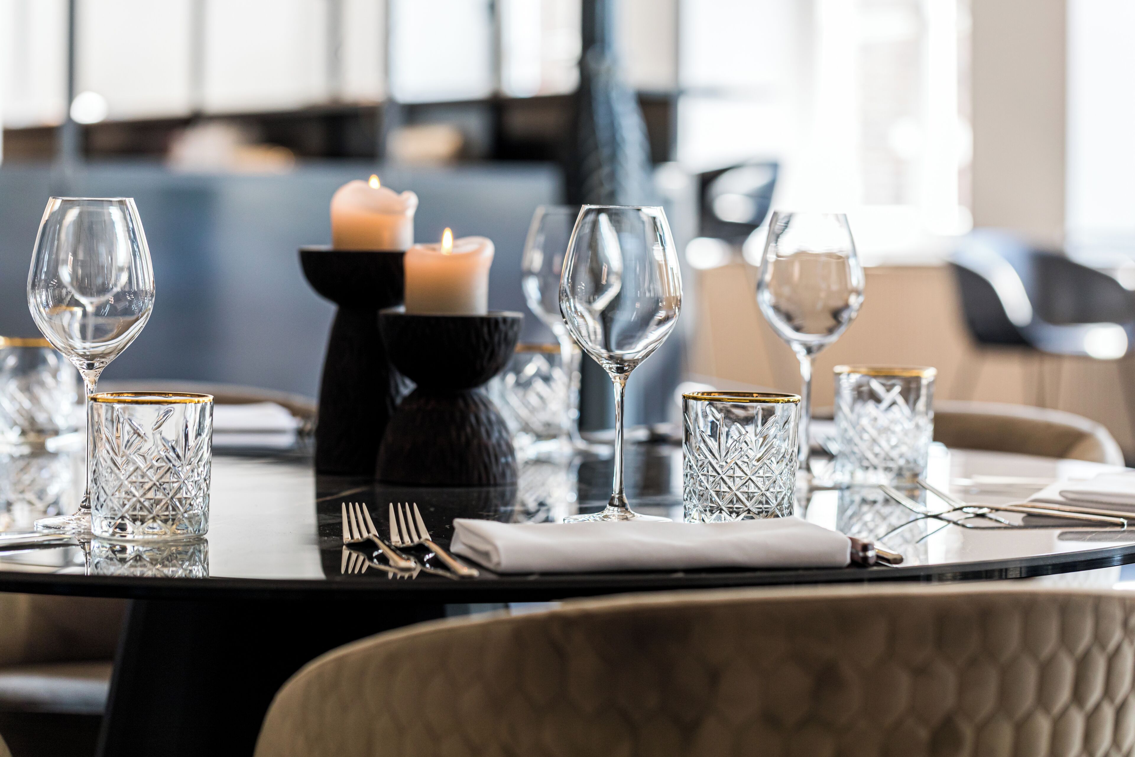 Una mesa de comedor dispuesta con copas de vino, una vela y cubiertos.