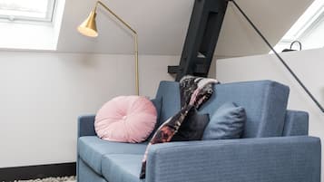 Un sofá azul con un cojín rosa y negro, una lámpara de pie dorada y una escalera negra contra una pared blanca.