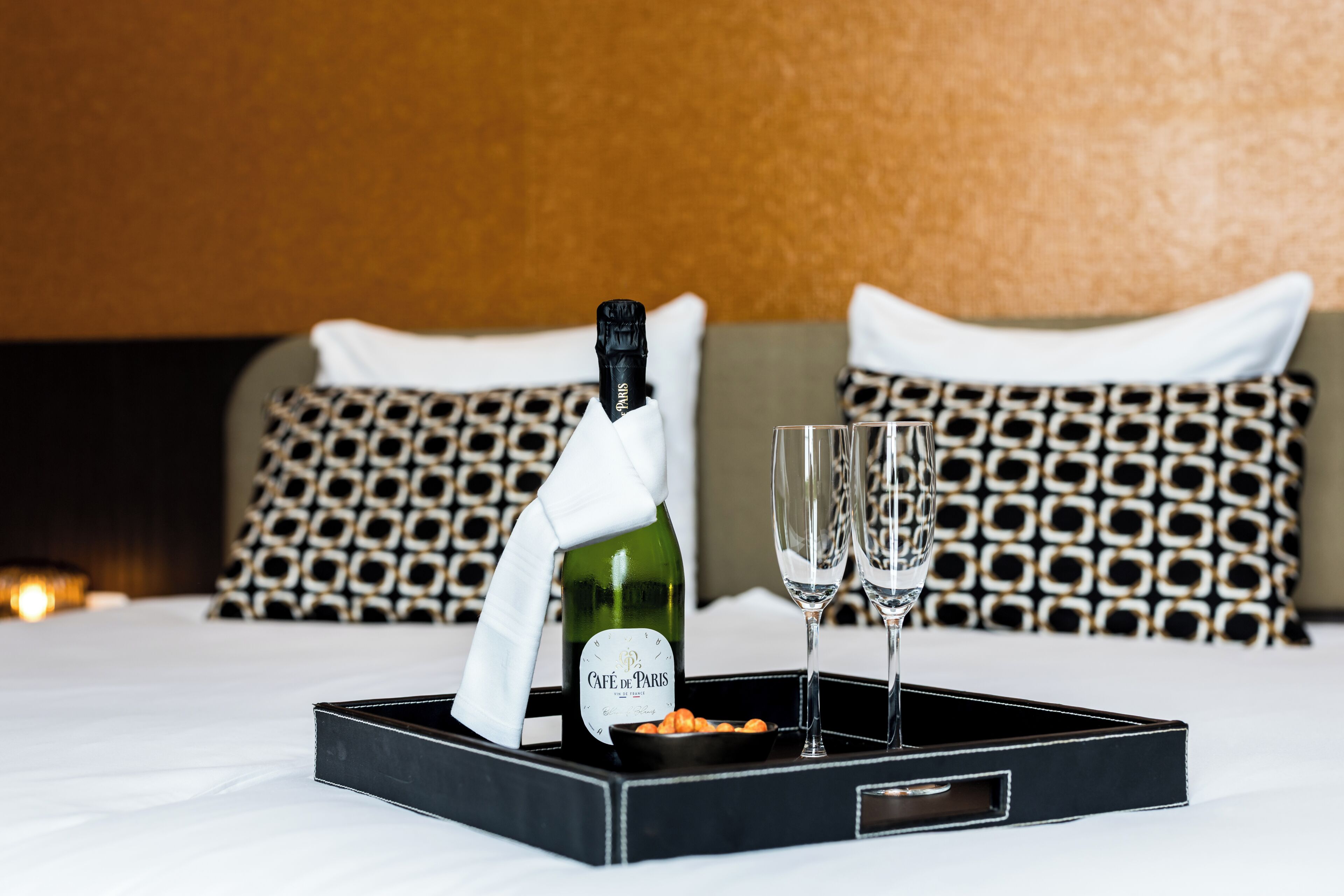 Una cama con una bandeja que contiene una botella de vino, copas y aperitivos.
