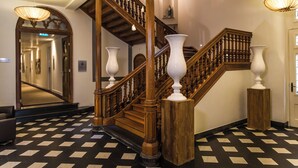 Una imponente escalera con barandas de madera y jarrones blancos en la base.