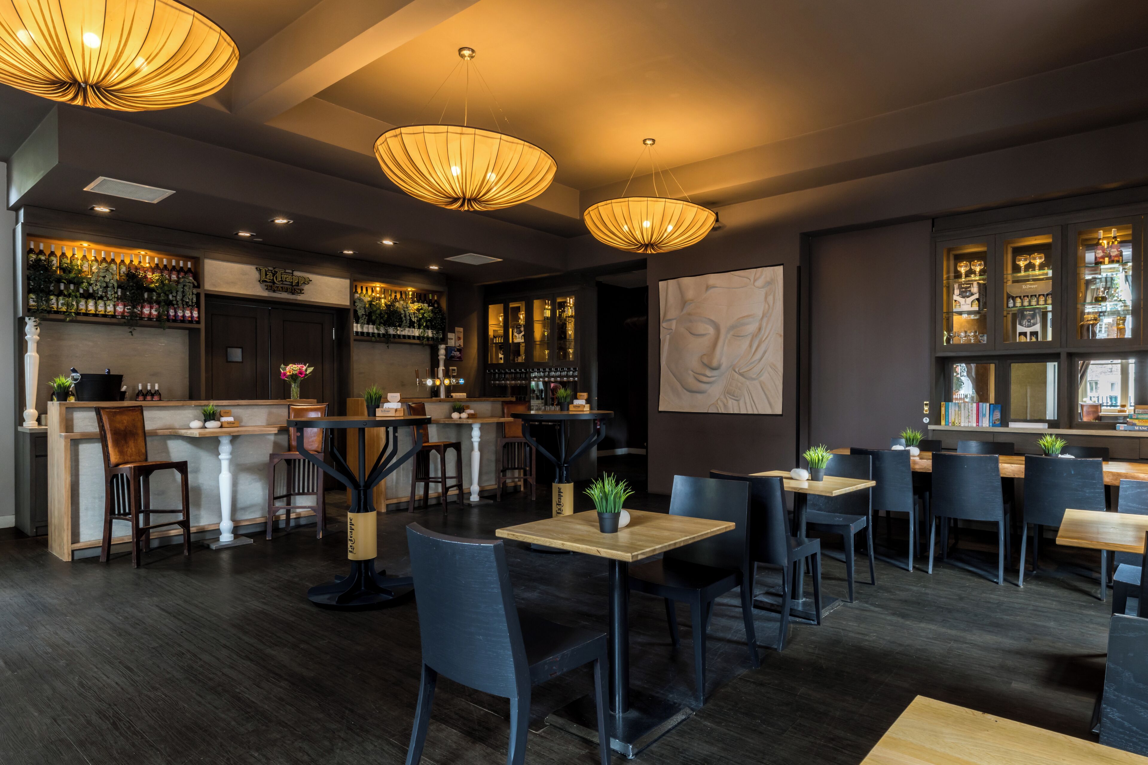 Un interno di ristorante con un'area bar, tavoli in legno, sedie nere e lampade a sospensione.