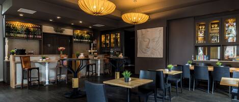 Un interno di ristorante con un'area bar, tavoli in legno, sedie nere e lampade a sospensione.