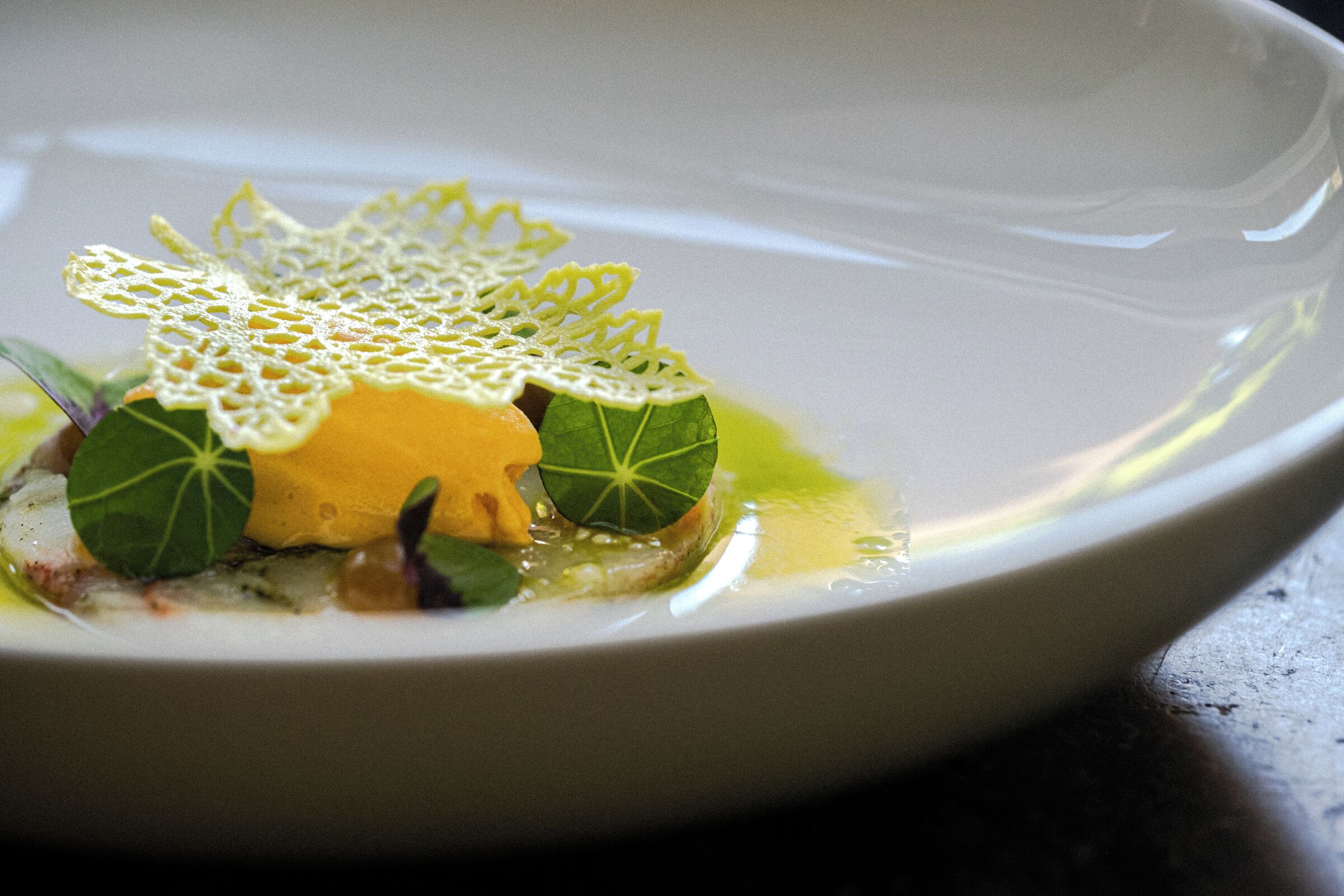 A white plate with a yellow sauce centerpiece, green leaves, and a delicate lace garnish.