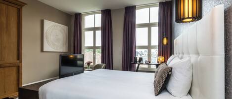 A modern hotel room with a large bed, a flat-screen TV, a dining table, and a view of the city.
