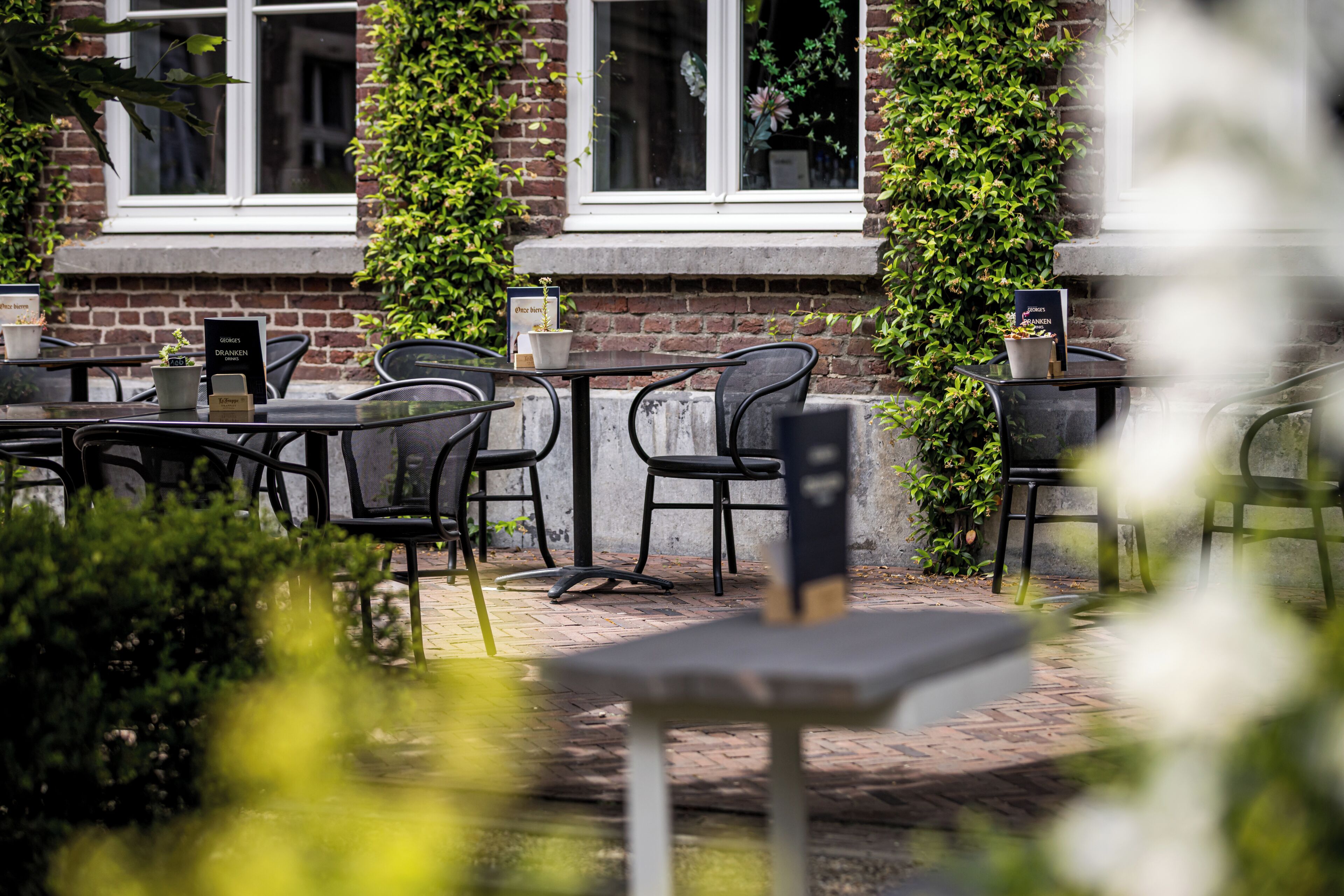 An outdoor seating area with tables and chairs, a brick wall, and a window with a view.