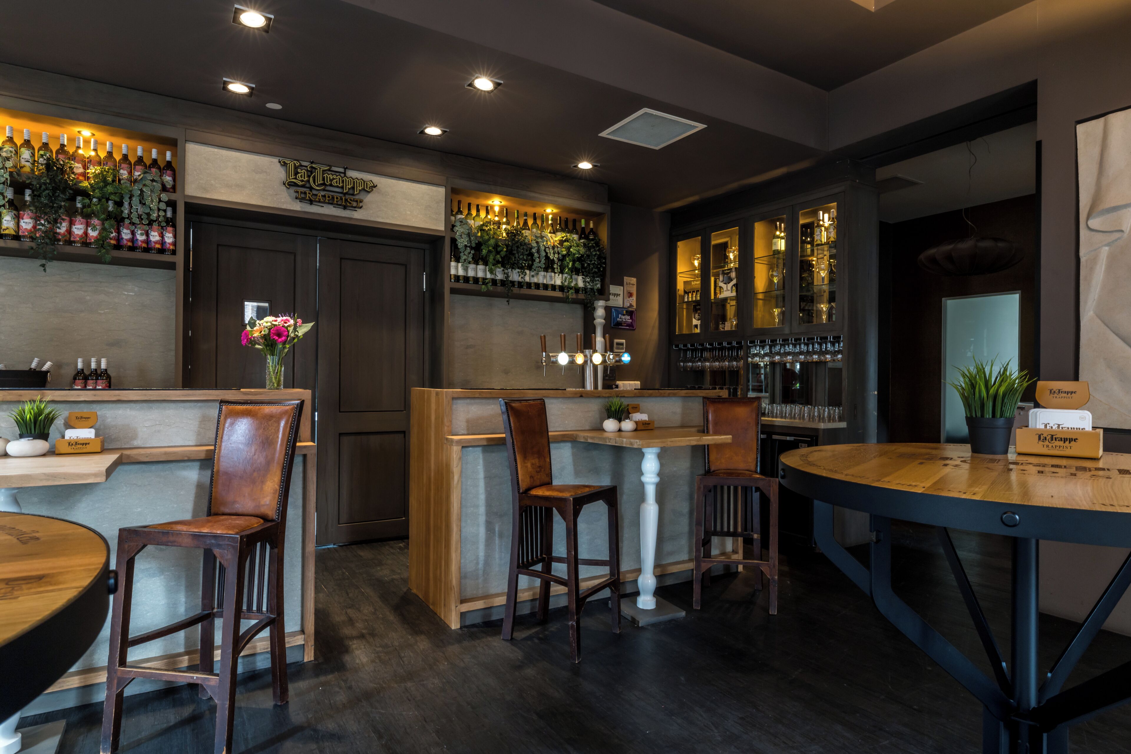 Una zona de bar con mobiliario de madera, barra y una variedad de botellas y vasos.