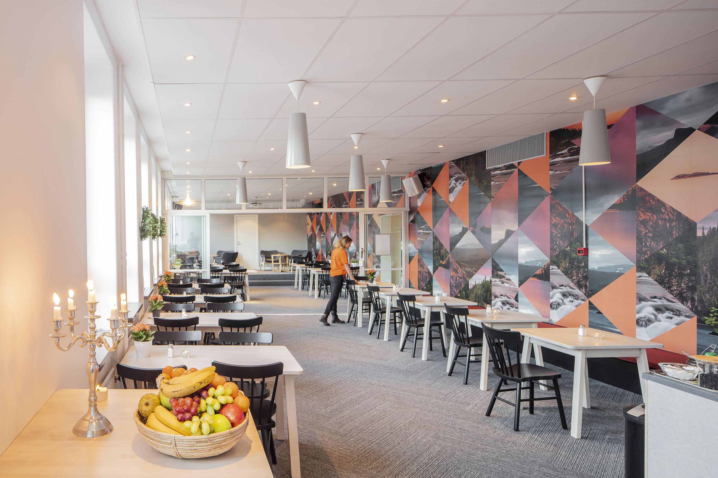 A modern dining area with tables and chairs, a fruit basket, and a candelabra.