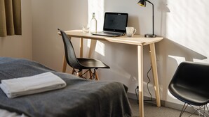 Una habitación de hotel con un escritorio de madera, una computadora portátil, una lámpara, una silla y una cama con manta.